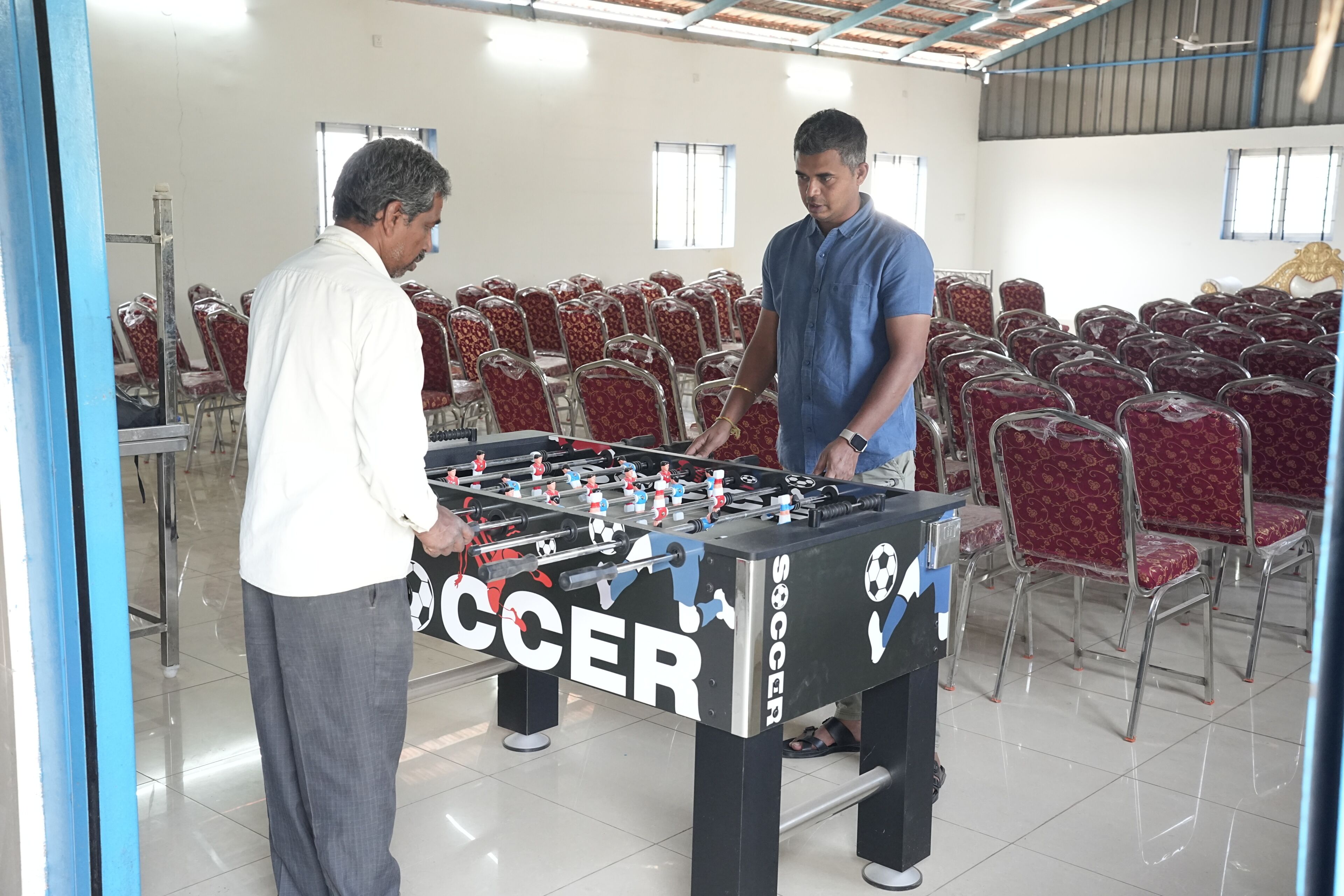 Una habitación con una mesa de fútbol de mesa, sillas rojas con estampado y piso de baldosas.