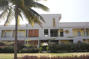 A multi-story building with a flat roof, large windows, and a central courtyard with a palm tree. - Royal Roots Resorts (Bengaluru)