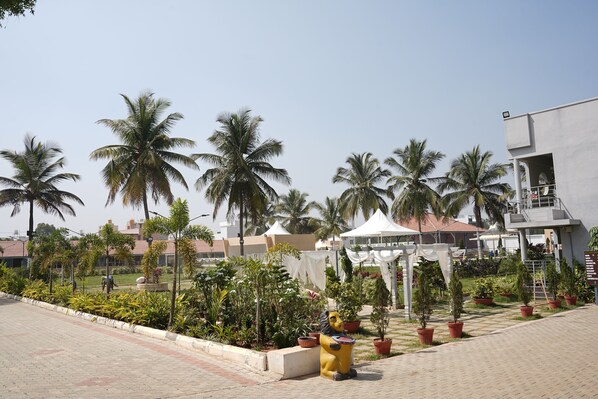 A paved outdoor area with palm trees, a yellow sculpture, and a building with a balcony.