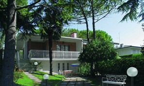 Ein zweistöckiges Haus mit Balkon, ein kleiner Garten mit Bank und Tisch mit buntem Sonnenschirm.