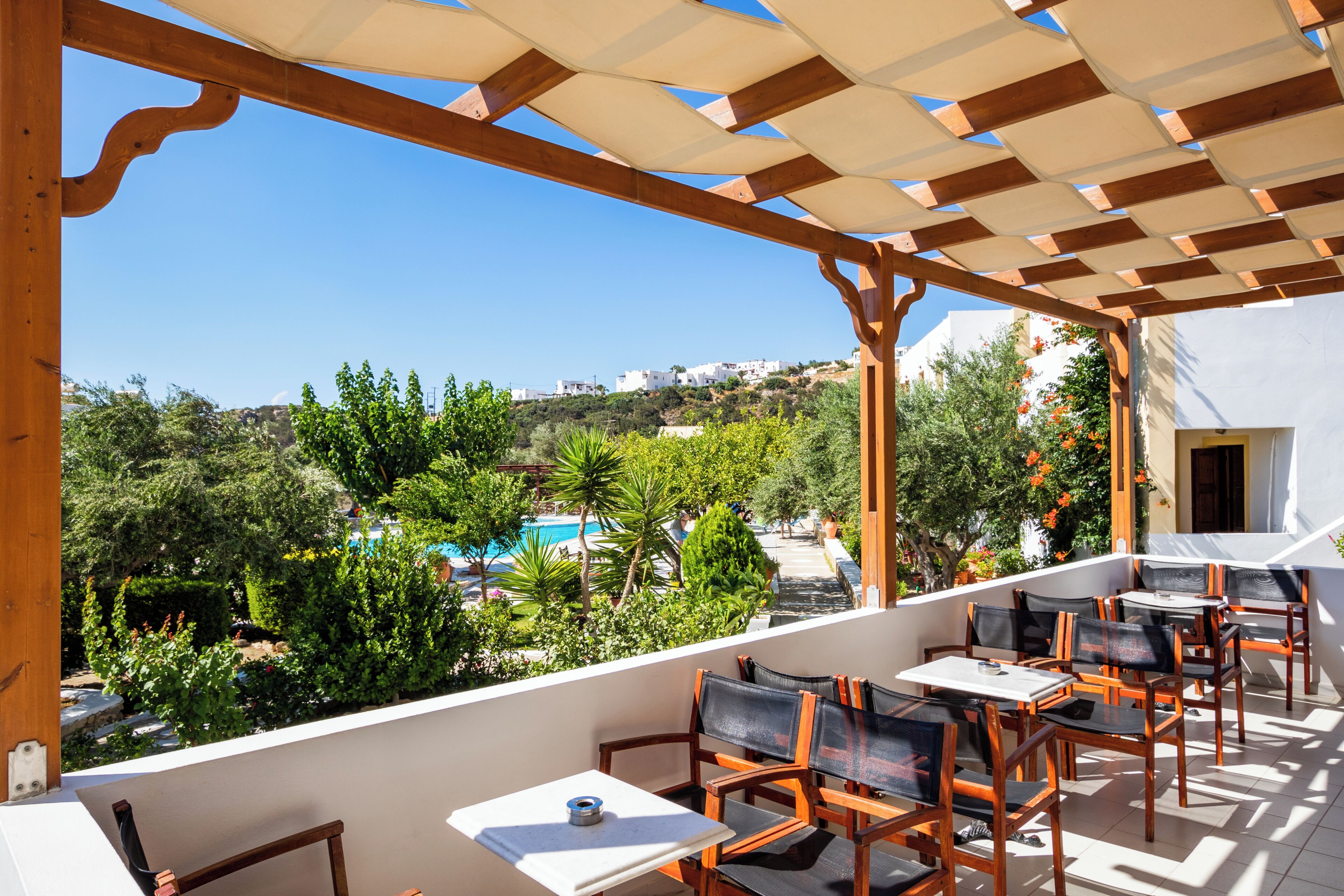 Una terraza con sillas y mesas de madera, con vistas a una piscina y follaje.