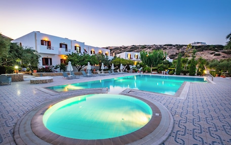 A pool area with lounge chairs, a circular hot tub, and a building with multiple balconies.