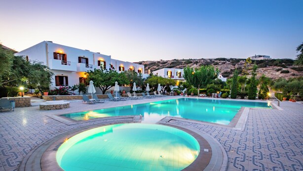 A pool area with lounge chairs, a circular hot tub, and a building with multiple balconies. - Casa Garden (Karpathos)