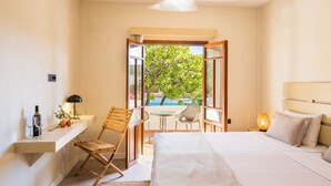 A bedroom with a bed, a desk with a lamp, a chair, and a view of a swimming pool. - Casa Garden (Karpathos)