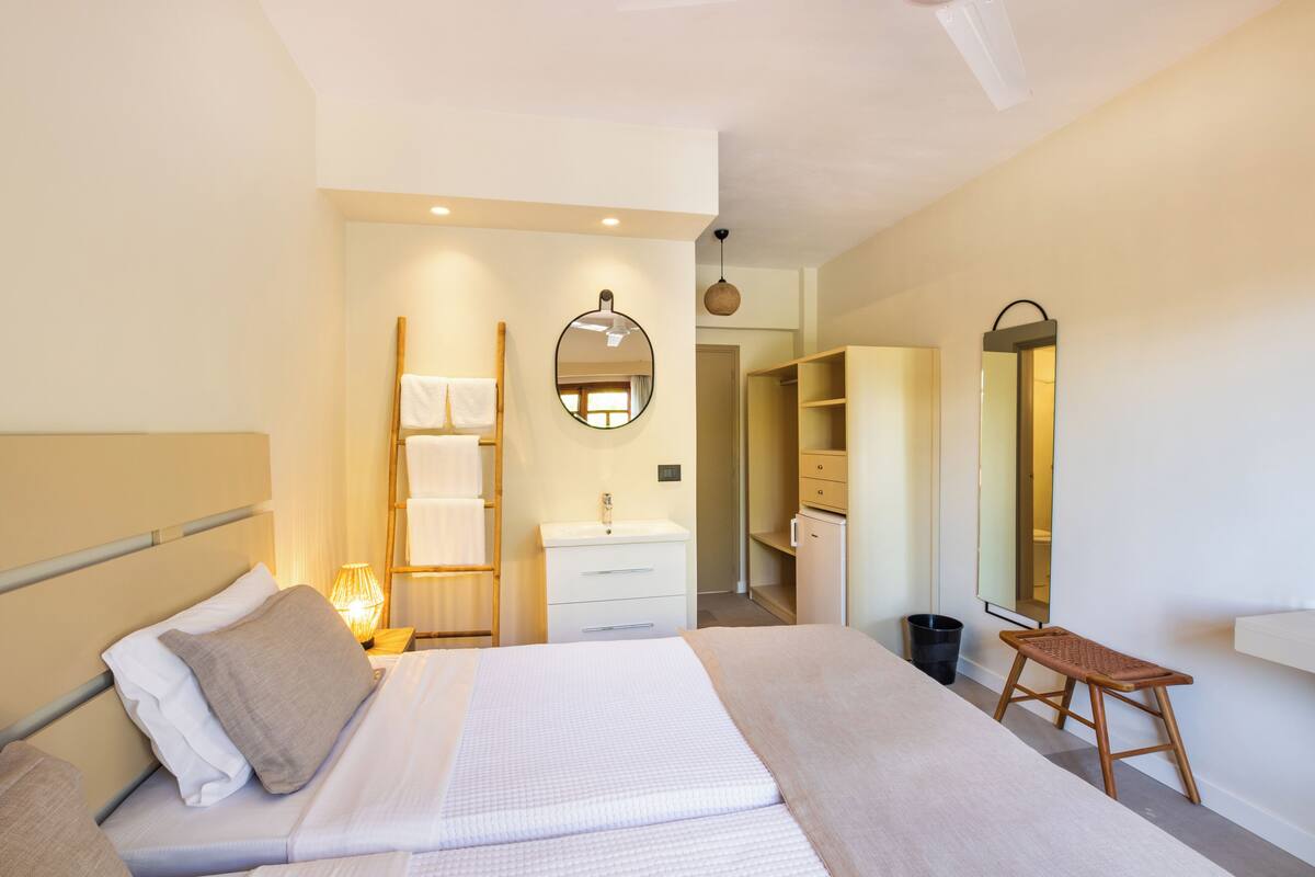 Ein Hotelzimmer mit Bett, Nachttisch, Spiegel, Kleiderschrank und Badezimmer mit Waschbecken und Handtuchhalter.