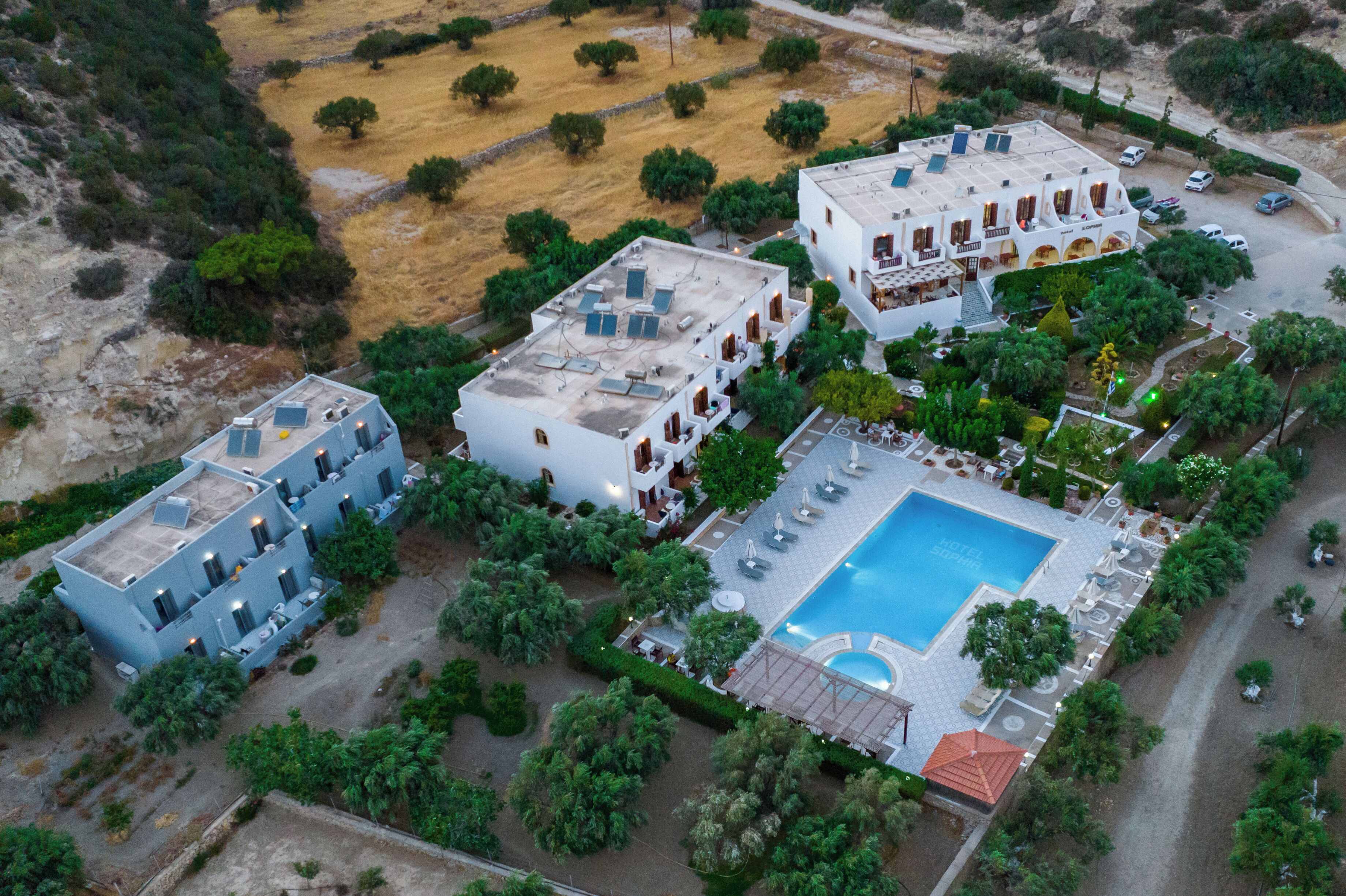 Vista aérea de un hotel con varias construcciones, piscina y vegetación circundante.