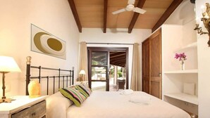 A bedroom with a bed, a nightstand, a lamp, a decorative item, a ceiling fan, and a view through a door. - Villa Jacobus (Pollença)