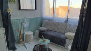 Tunnelmallinen huone, jossa on kuviollinen sohva, lattiatuuletin, pieni pöytä, jossa on kynttilä, ja koristeellinen maljakko.