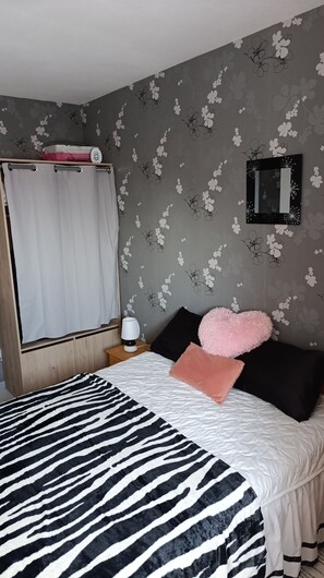 Ein Schlafzimmer mit einem Bettbezug mit ZEBRA-MUSTER, einem weißen Vorhang, einem Spiegel und blumengemusterten Tapeten.