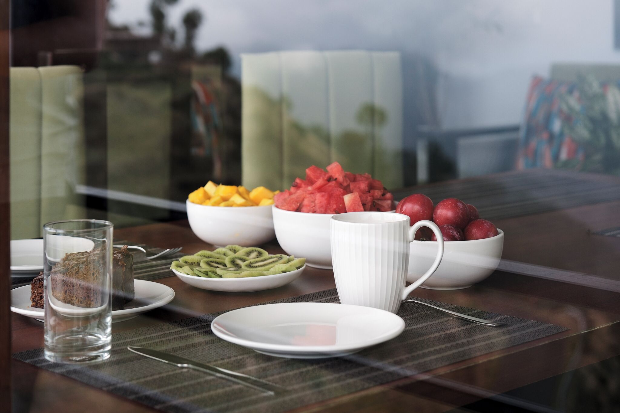 A dining table with various fruits, a white mug, and a glass of water.