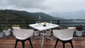 Eine Terrasse mit Tisch für zwei Personen, umgeben von weißen Stühlen, Blumentöpfen und einem herrlichen Bergblick.