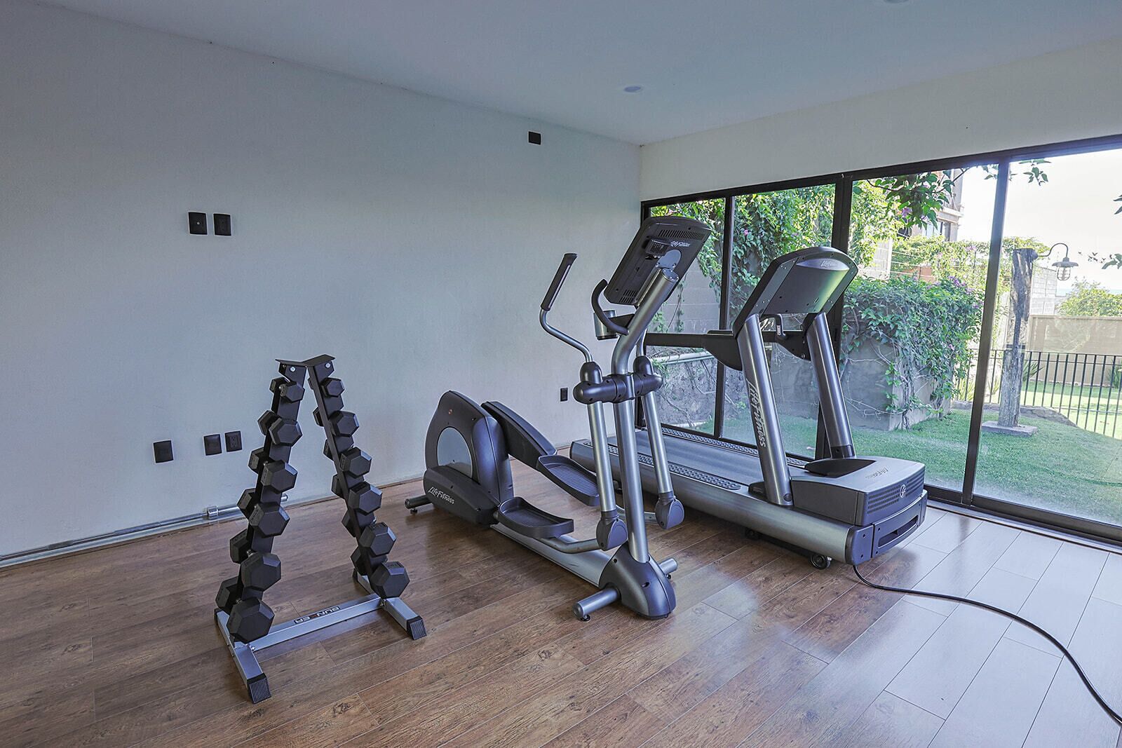 A gym with a treadmill, elliptical, and dumbbells.