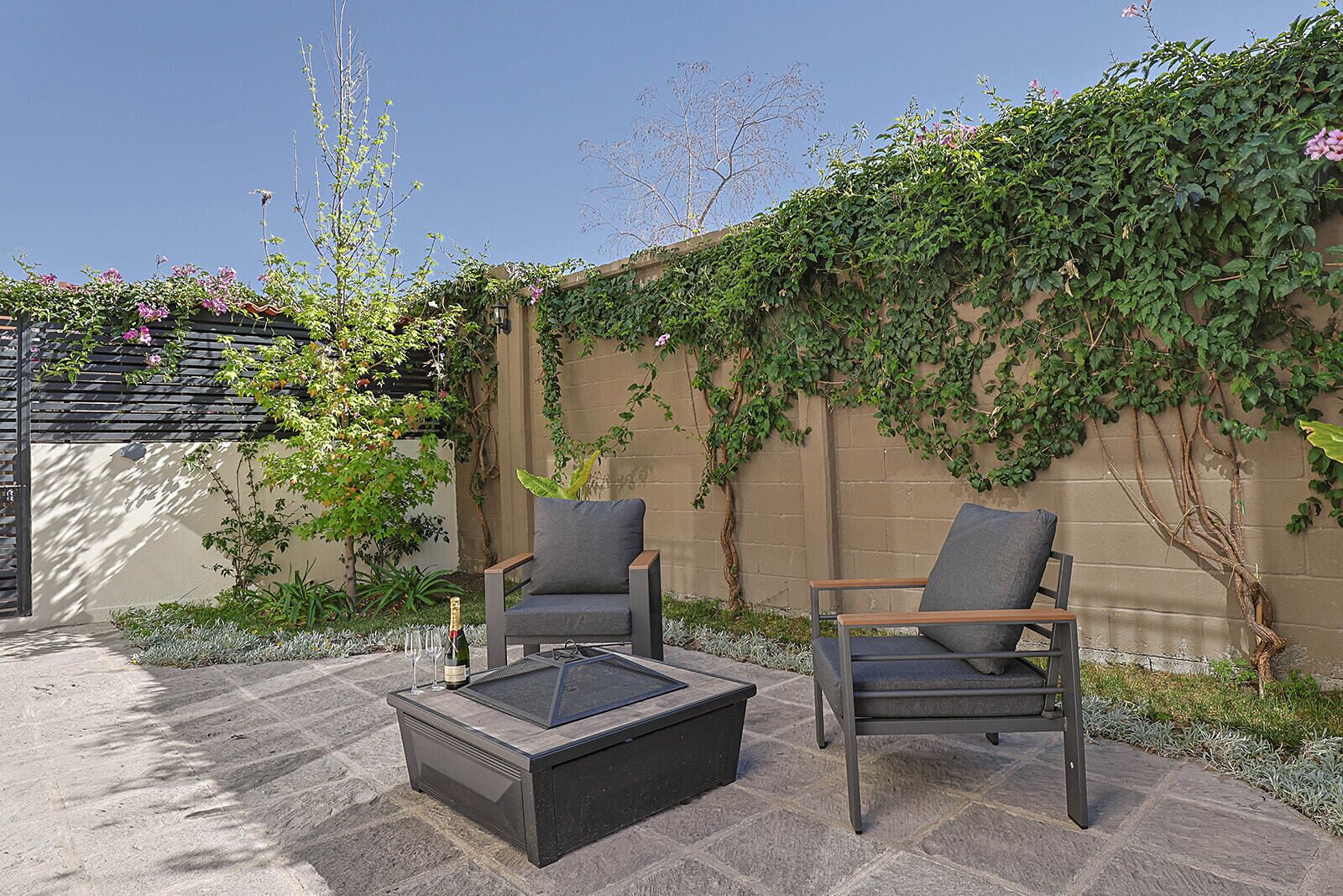 An outdoor seating area with two chairs and a table, surrounded by a brick wall and greenery.