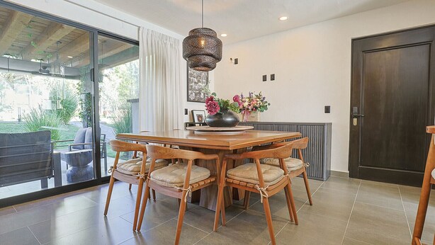 A dining area with a wooden table and chairs, a hanging light fixture, and a view through a glass door.