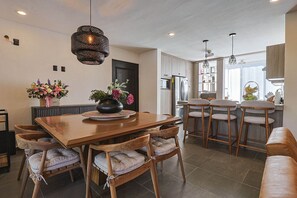 Una cucina moderna con zona pranzo, caratterizzata da un tavolo in legno, sgabelli da bar e illuminazione a sospensione.