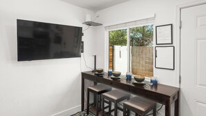 A kitchen with a flat-screen TV mounted on the wall, a window with a view of the outside, and a bar area with stools. - Desert Rose Retreat in the Heart of Downtown PHX (Phoenix)