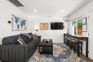 Ein moderner Wohnbereich mit Sofa, Couchtisch, Fernseher und einem Essbereich mit Stühlen.