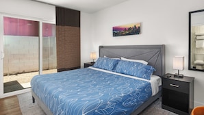 A bedroom with a bed, a nightstand, a lamp, a cityscape painting, and a sliding glass door. - Desert Rose Retreat in the Heart of Downtown PHX (Phoenix)