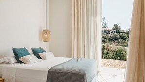 Une chambre à coucher avec un lit, des oreillers, une table de chevet, un luminaire suspendu et une vue sur l’extérieur.