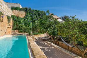 A pool with a stone wall, a hammock, and a tree with green leaves. - Villa Alaior with private pool - My Rental Homes (Alaior)