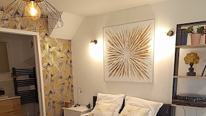 A modern bedroom with a bed, bedside tables, a nightstand, a wall-mounted light, and a decorative wall piece. - Charming studio in the heart of the mountains (Burzet)