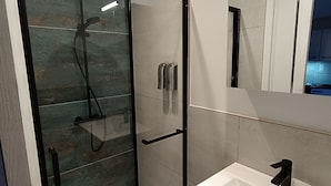 A modern bathroom with a glass-enclosed shower, a white sink, and a mirror above it. - Charming studio in the heart of the mountains (Burzet)