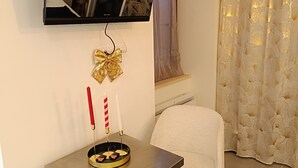 A modern living room with a flat-screen TV mounted on the wall, a small round table with candles, and a white armchair. - Charming studio in the heart of the mountains (Burzet)
