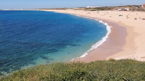 Una spiaggia costiera con acque blu cristalline, una riva sabbiosa e edifici in lontananza.