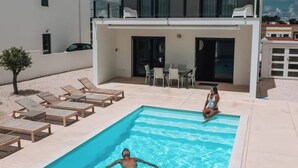 Un edificio moderno su due piani con piscina, sedie a sdraio e zona pranzo.