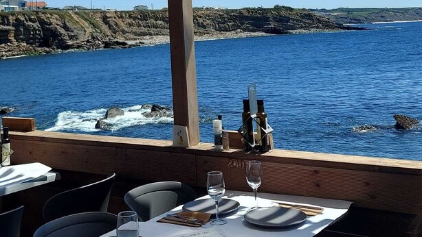 Un ristorante sul mare con posti a sedere all'aperto, vista sull'oceano e una pergola in legno.