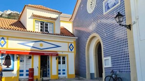 Una piazza lastricata con un edificio caratterizzato da piastrelle a motivi blu e bianchi, una bicicletta e una vetrina con tenda rossa.
