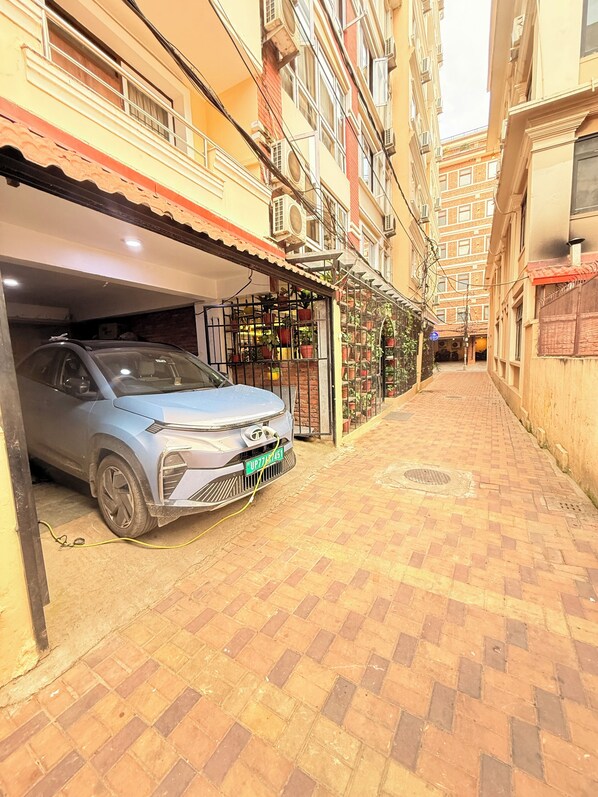 A narrow alleyway with a parked car, a gated entrance with potted plants, and multi-story buildings with balconies. - 14 LUXE By Mums Home (Kathmandu)