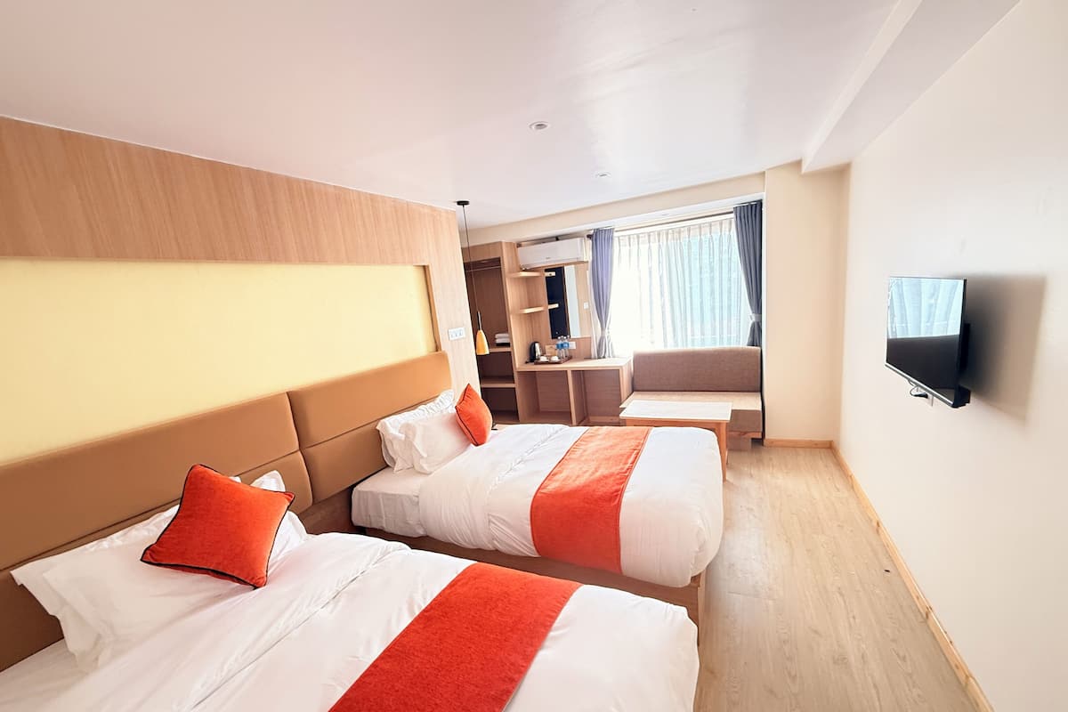 A hotel room with two beds, a desk, a TV, and a window with curtains.