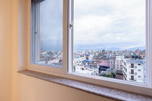 A window with a view of a densely packed urban area with various buildings and a cloudy sky. - 14 LUXE By Mums Home (Kathmandu)