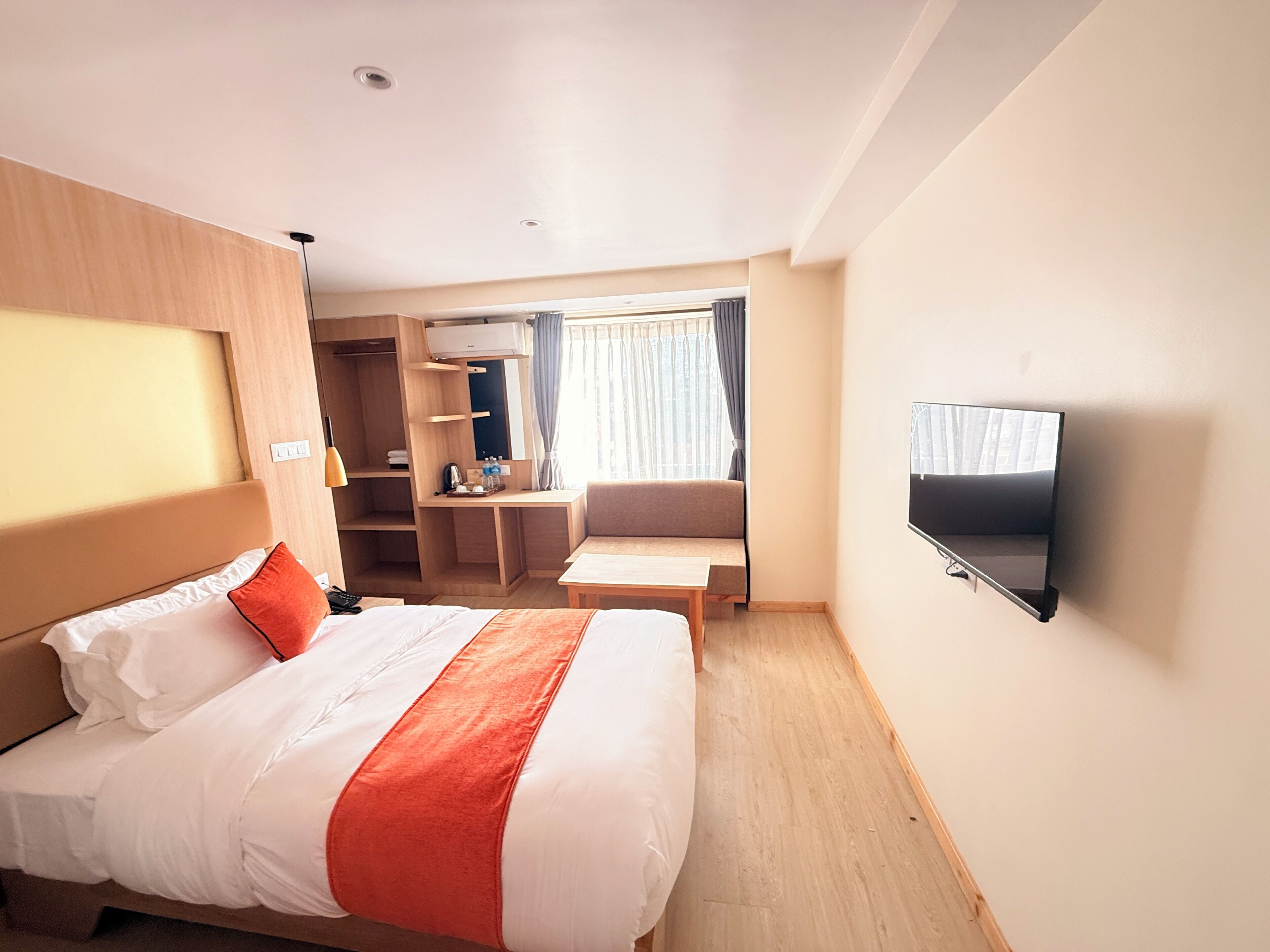 A hotel room with a bed, a desk, a TV, and a window with curtains.