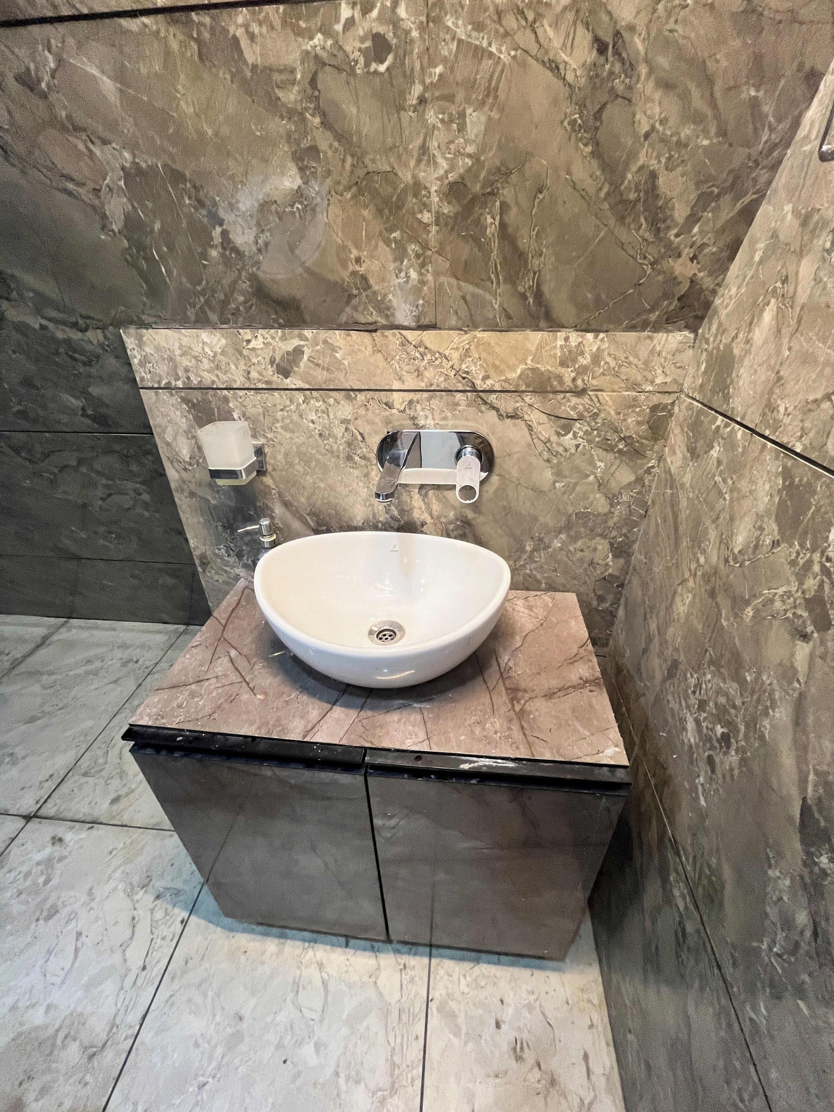 A bathroom with a marble sink, chrome faucet, and a soap dispenser.