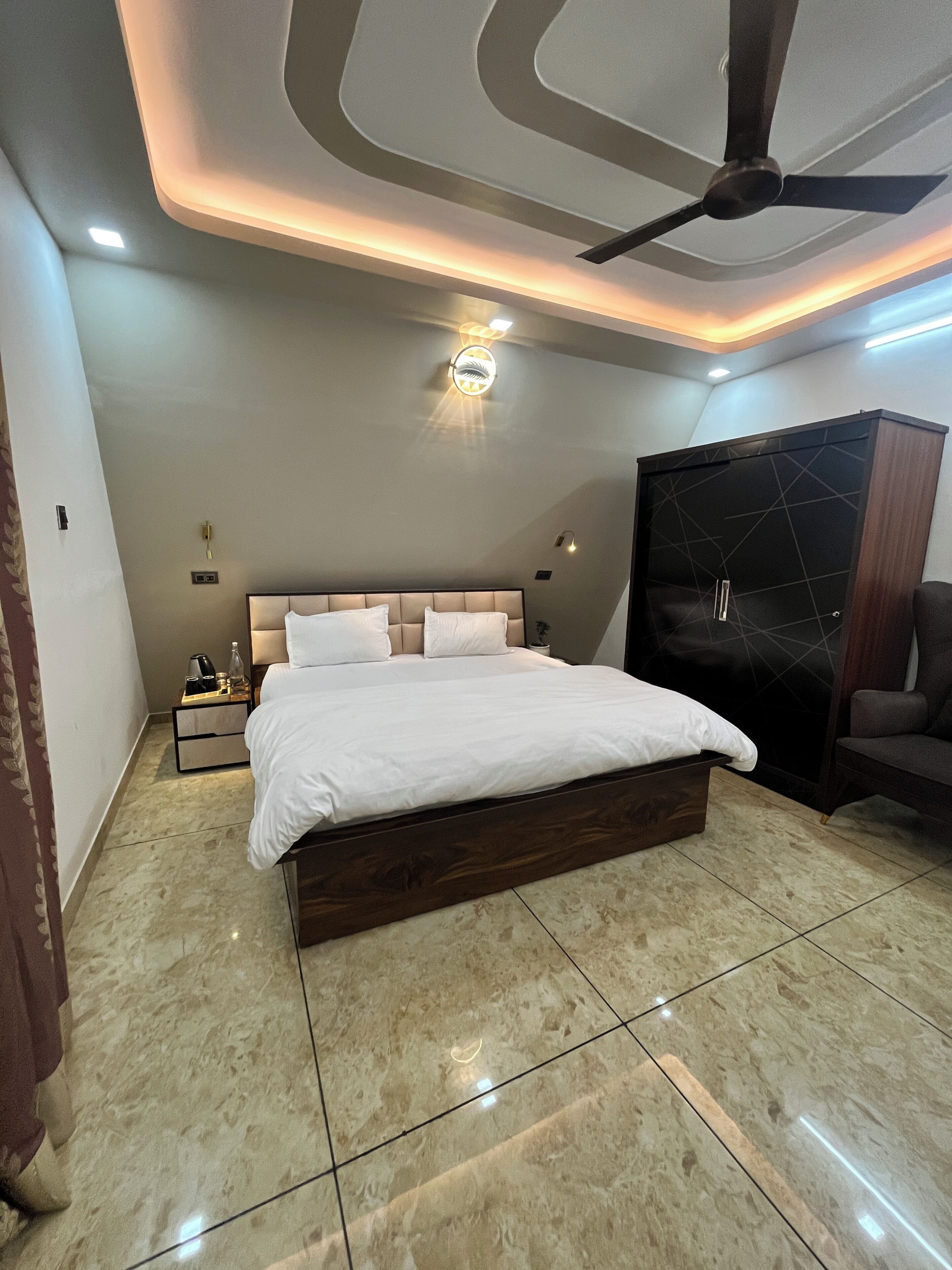 A modern bedroom with a large bed, a ceiling fan, recessed lighting, a wardrobe, and a nightstand.