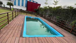 Eine Holzterrasse mit Swimmingpool, einem roten und blauen Gebäude und einer grünen Rasenfläche.