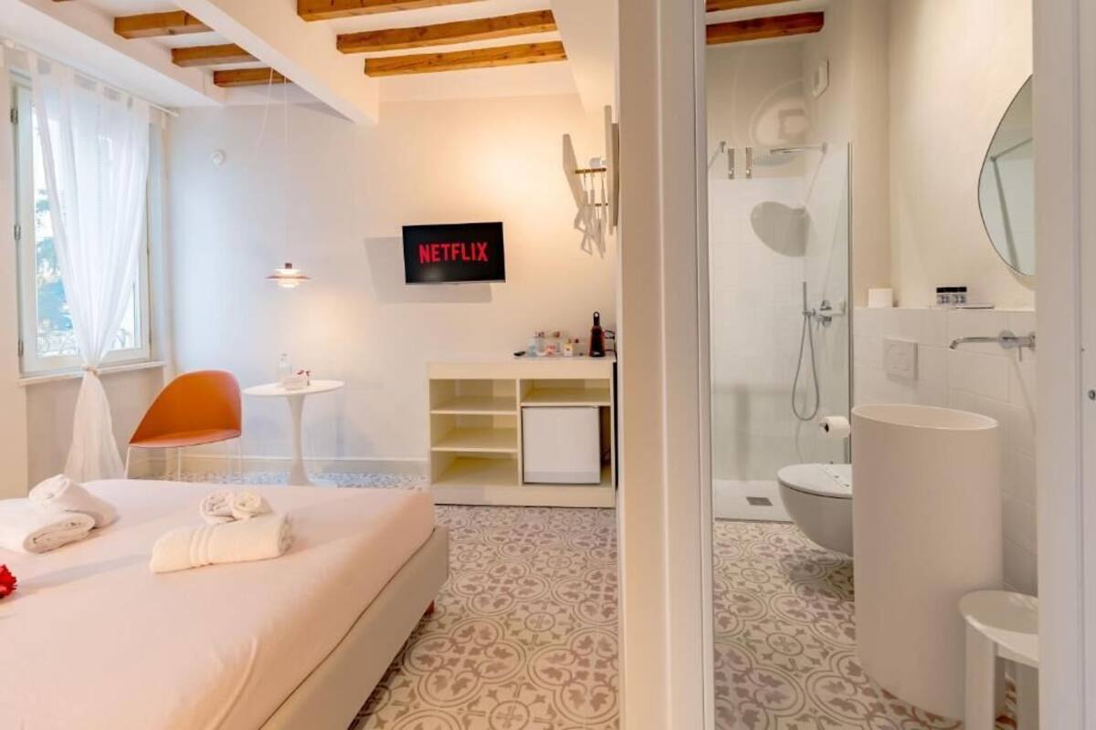 A hotel room with a bed, a small table, a chair, a TV, a shower, and a bathroom.