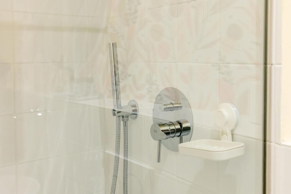 A shower with a handheld showerhead and a wall-mounted faucet.