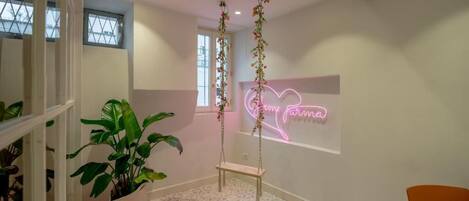 Une pièce décorée avec une plante suspendue, un néon, un banc et un revêtement de sol à motifs.
