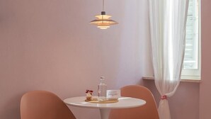 A room with a round table, two chairs, a hanging light fixture, a bottle, a small decorative item, and a window with curtains. - GLAM PARMA (Parma)
