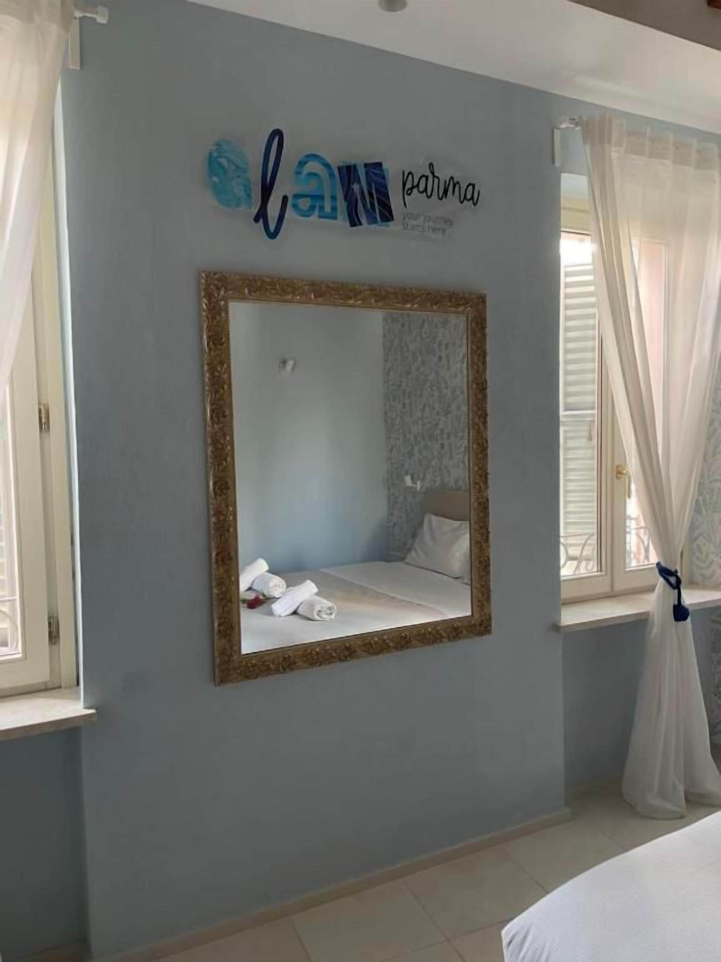 A bedroom with a large mirror, a bed, and a window with curtains.