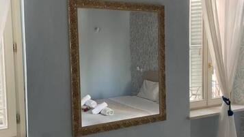 A bedroom with a large mirror, a bed, and a window with curtains.