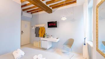 Een moderne hotelkamer met een houten plafond, een wit bureau, een televisie, een spiegel en een raam met gordijnen.