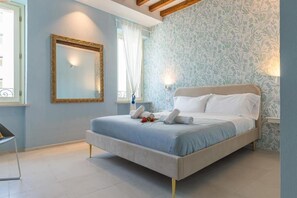 Une chambre à coucher avec un lit, un miroir, une fenêtre avec des rideaux et un mur orné d’un motif floral.