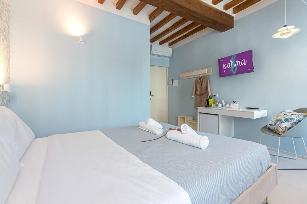 A bedroom with a bed, a desk with toiletries, a chair, and a TV on the wall.