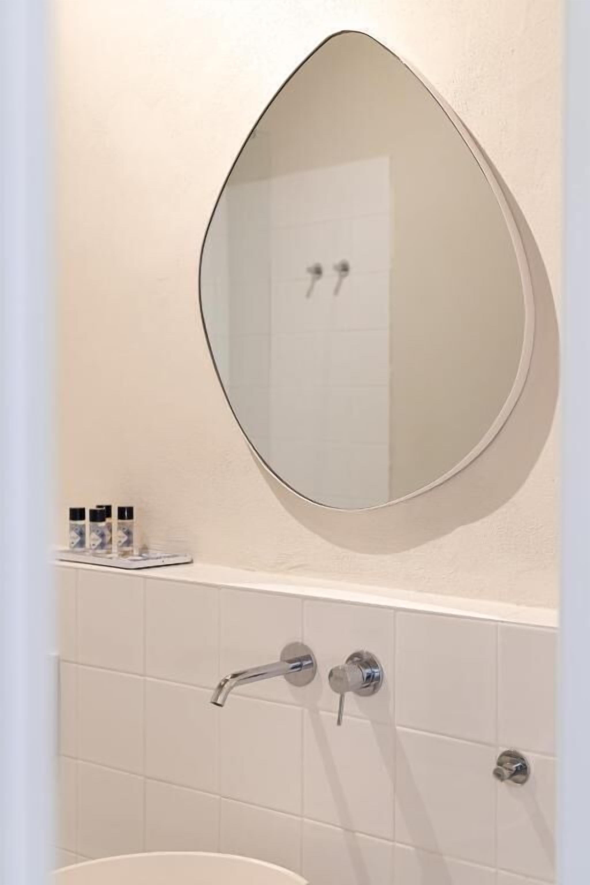 A bathroom with a round mirror, a white sink, and a tiled wall.