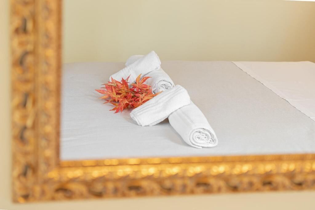 Una cama bien hecha con toallas blancas enrolladas y un arreglo decorativo de hojas rojas y anaranjadas.