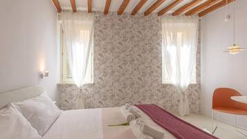 A hotel room with a bed, a small table, a chair, and a window with curtains.